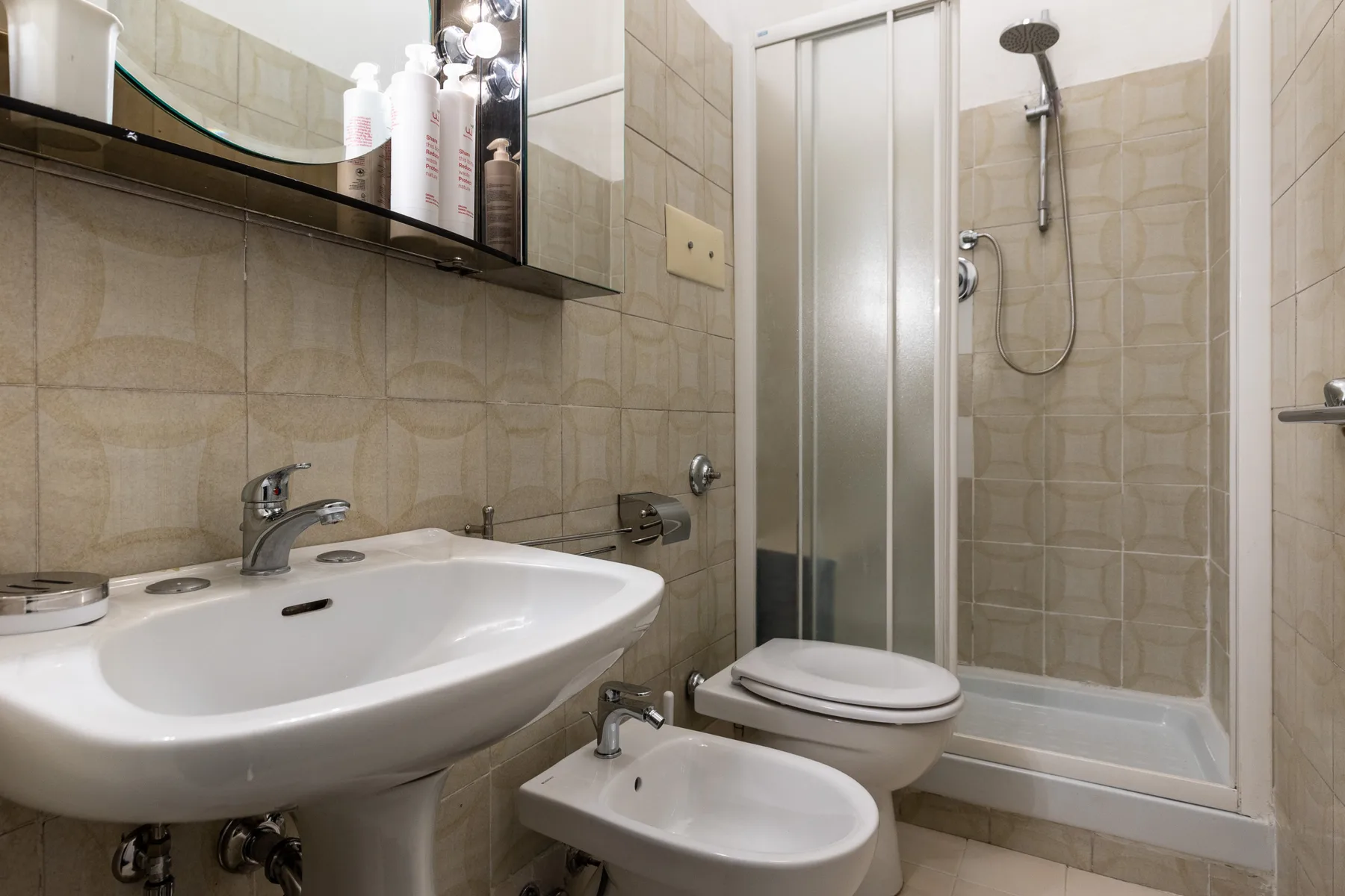A tiled bathroom with a sink, toilet, bidet, and shower.