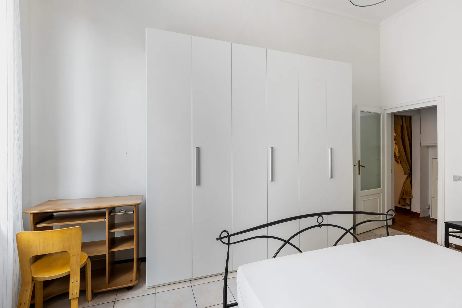 A bright bedroom with a bed, tall white wardrobes, and a small desk.