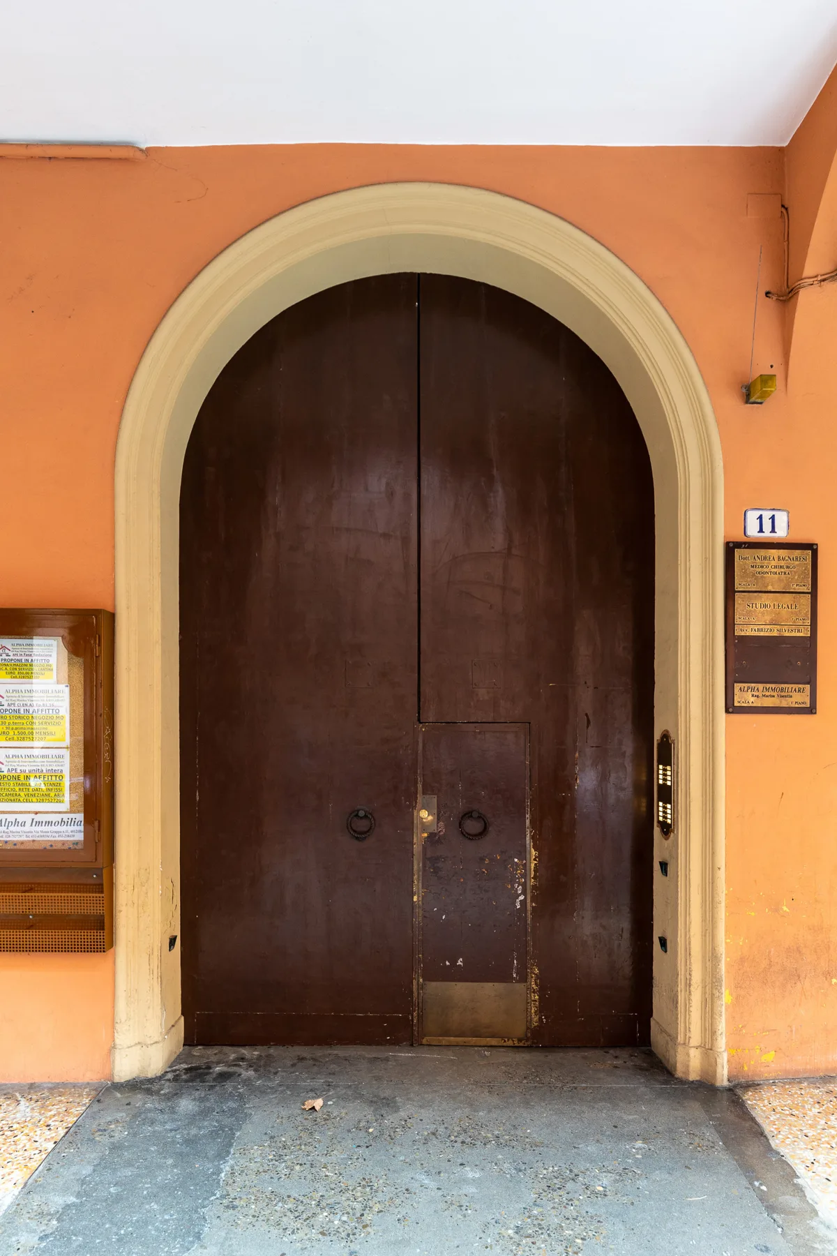 A tall dark wooden entrance door sits within an arched frame in an orange wall.