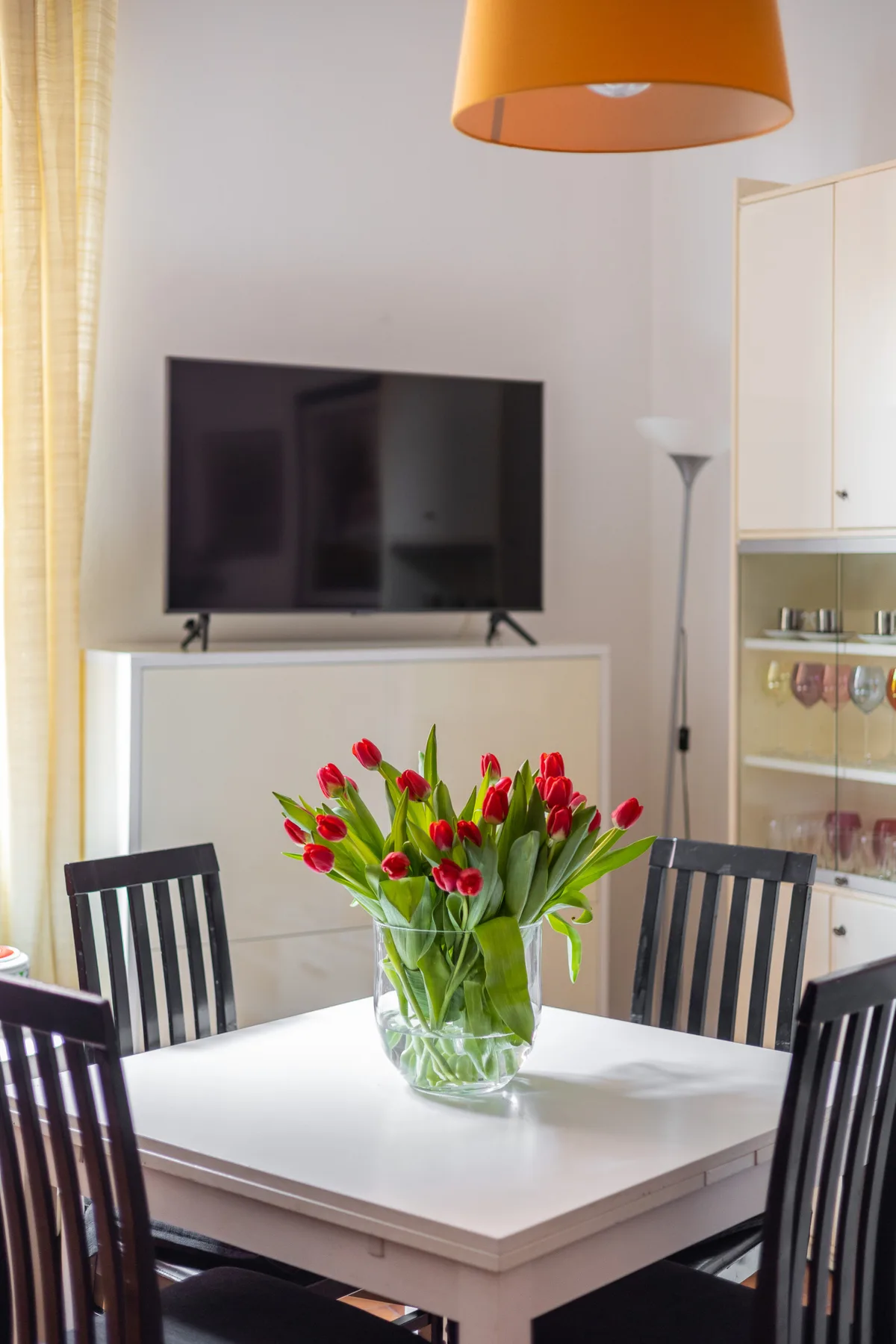 A dining area with a white table, dark seating, and a vase of red flowers.