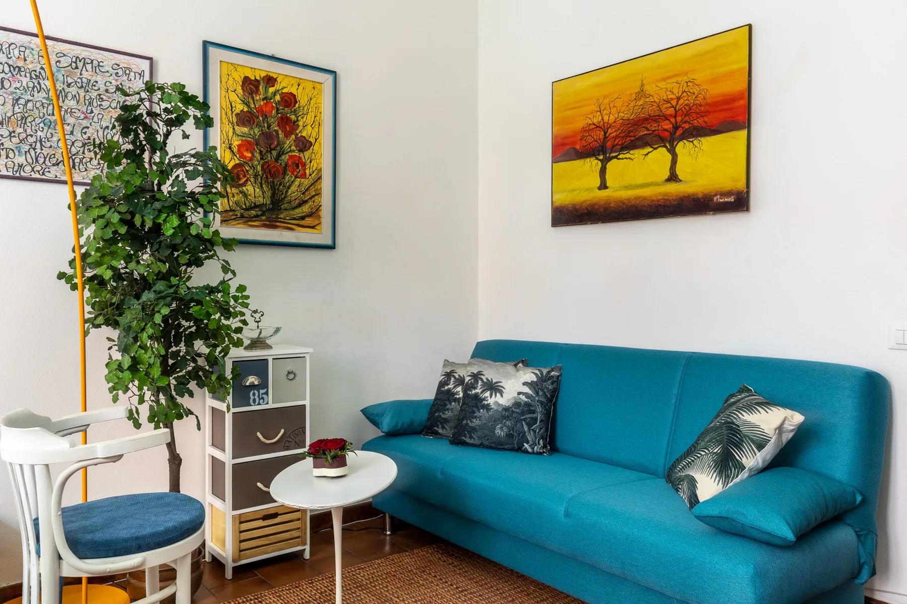 A bright living room features a teal sofa, framed artwork, and a leafy plant.