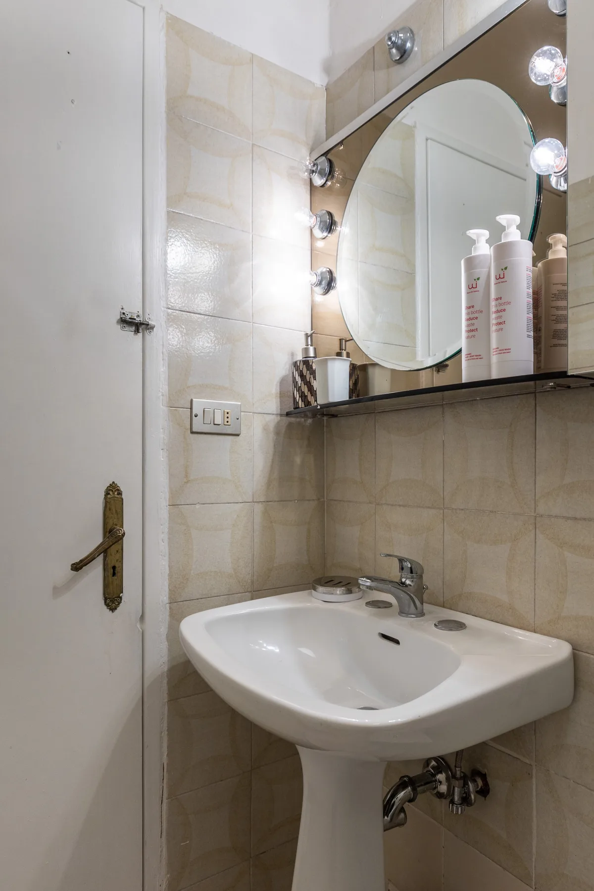 A tiled bathroom with a pedestal sink and a mirror above it.