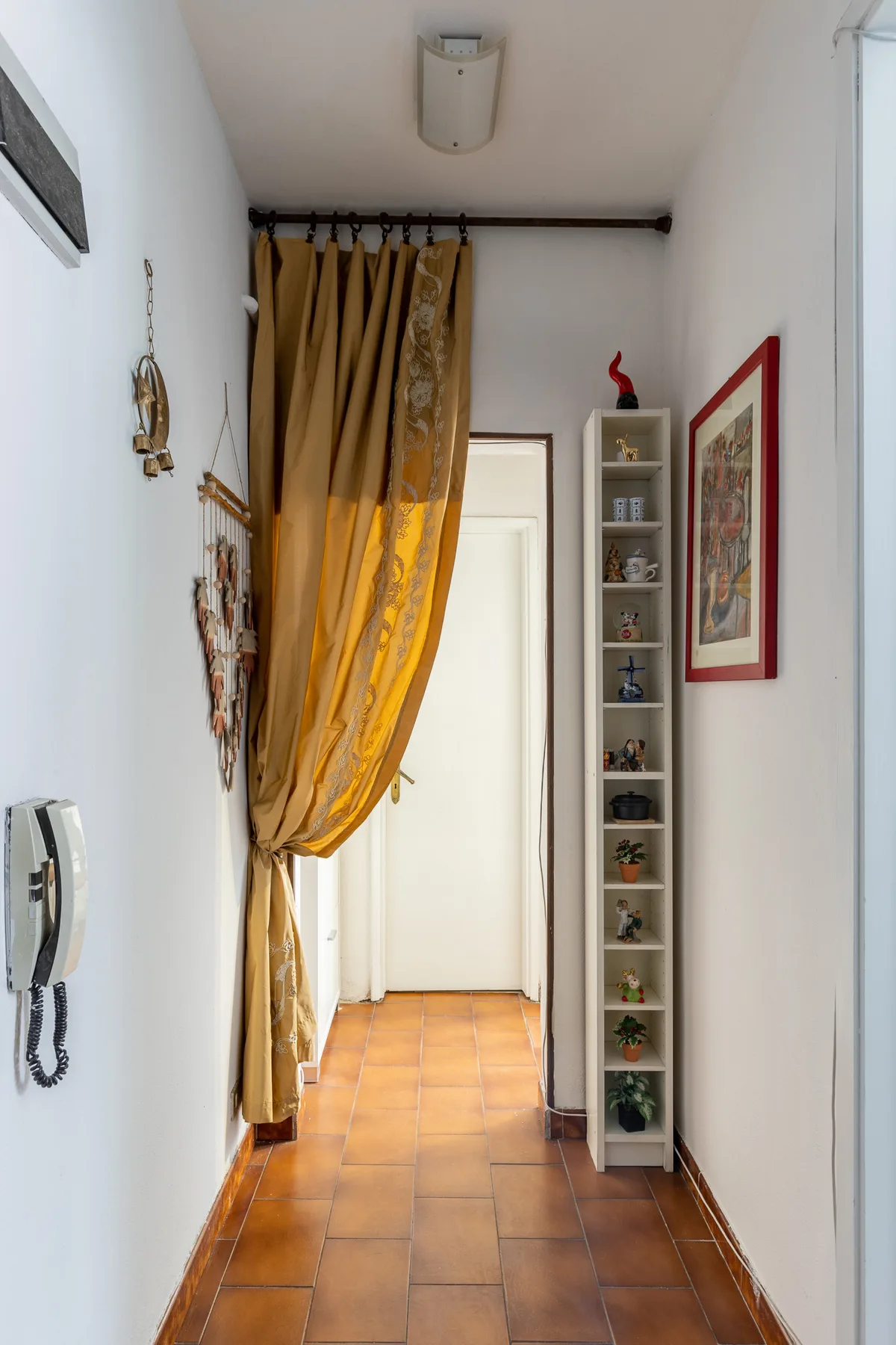 A narrow hallway with a golden curtain and a tall display shelf.