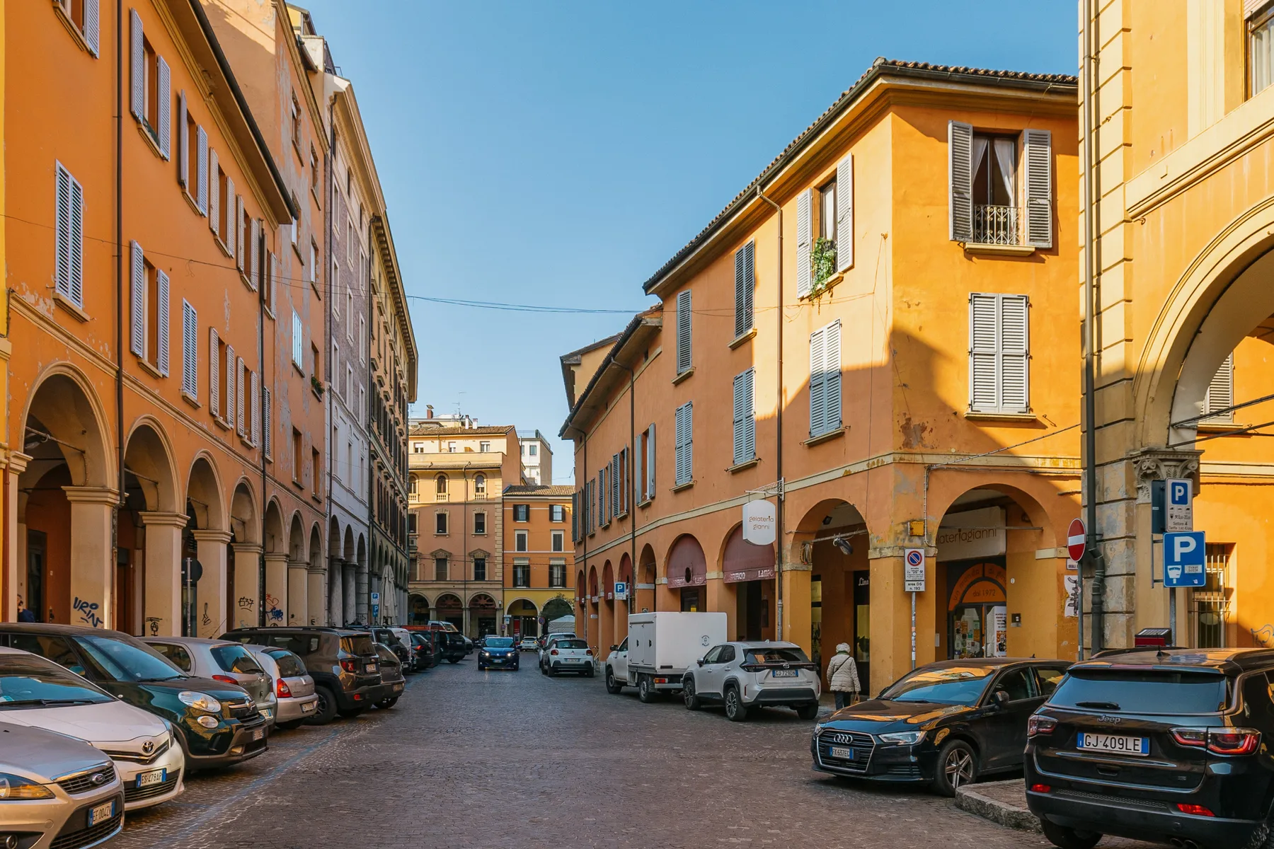 A narrow cobblestone street lined with colorful buildings and parked cars.