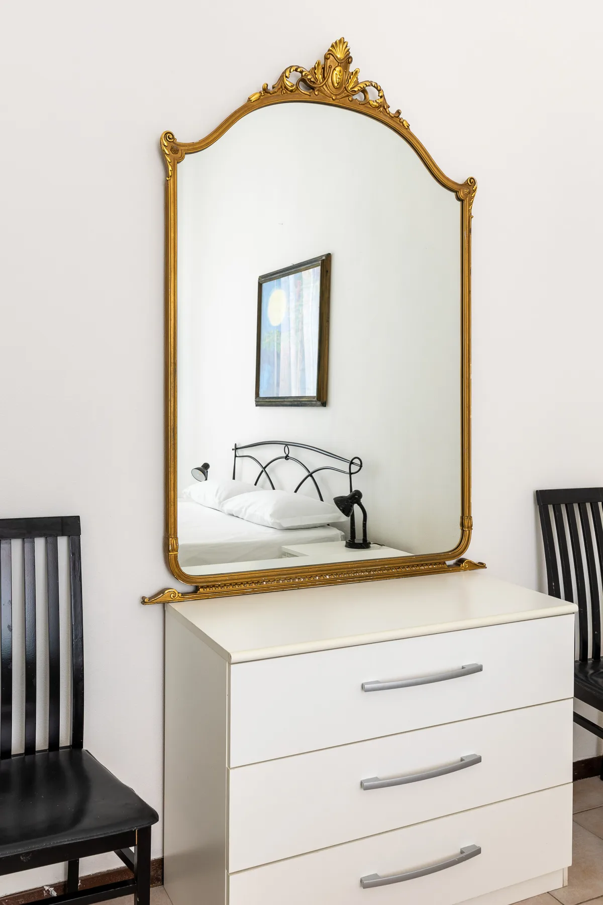 A white chest of drawers with an ornate gold-framed mirror above it.