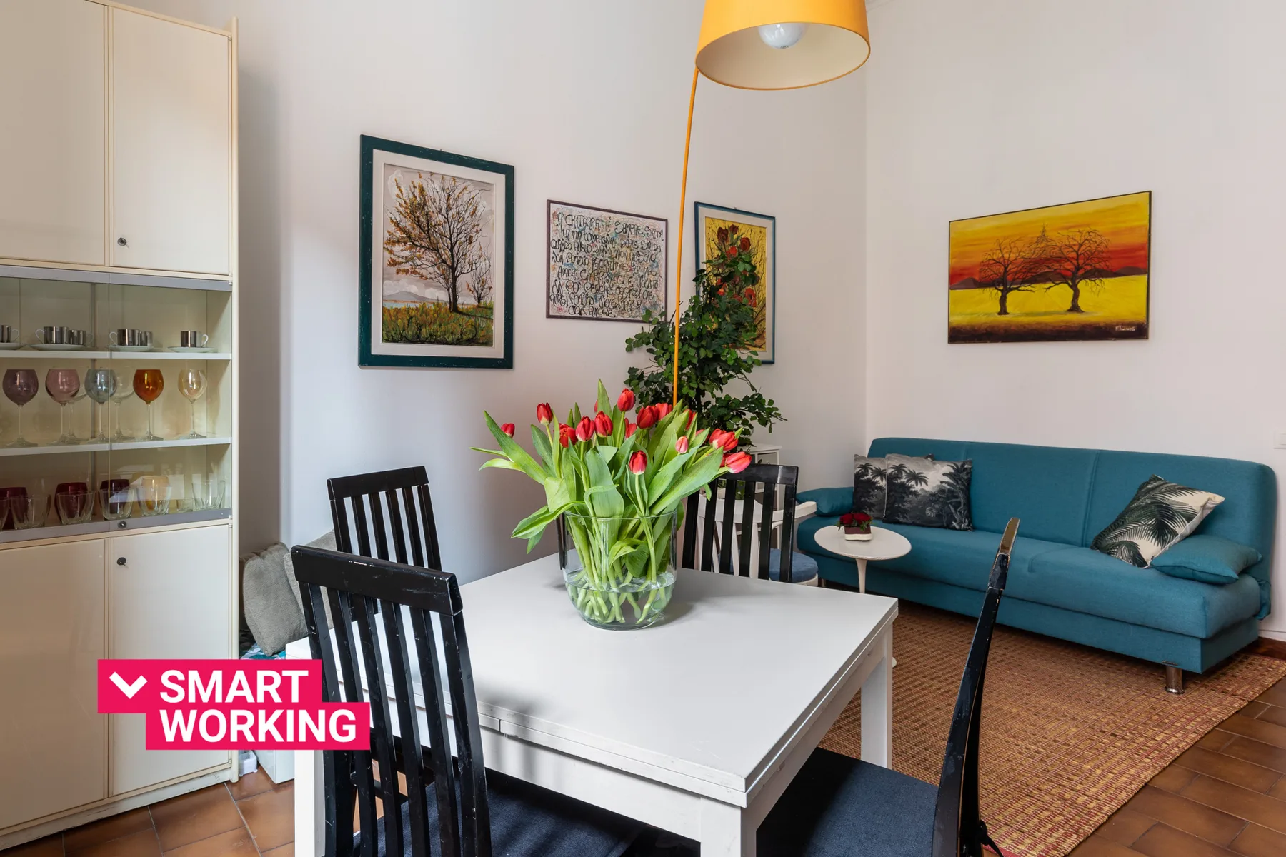 A dining area with a white table and colorful artwork above a blue sofa.