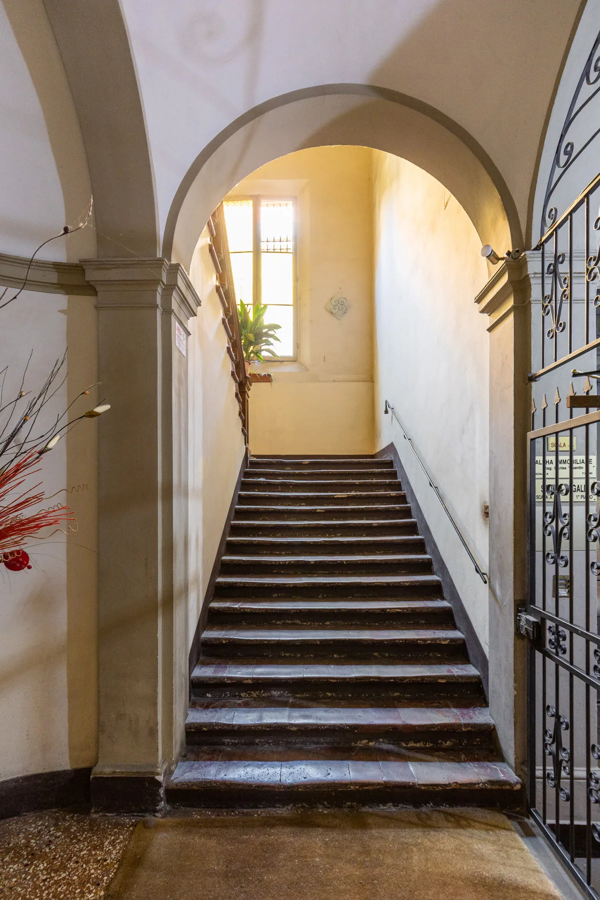 A stairwell rises beneath an arched opening, with a sunlit window above.