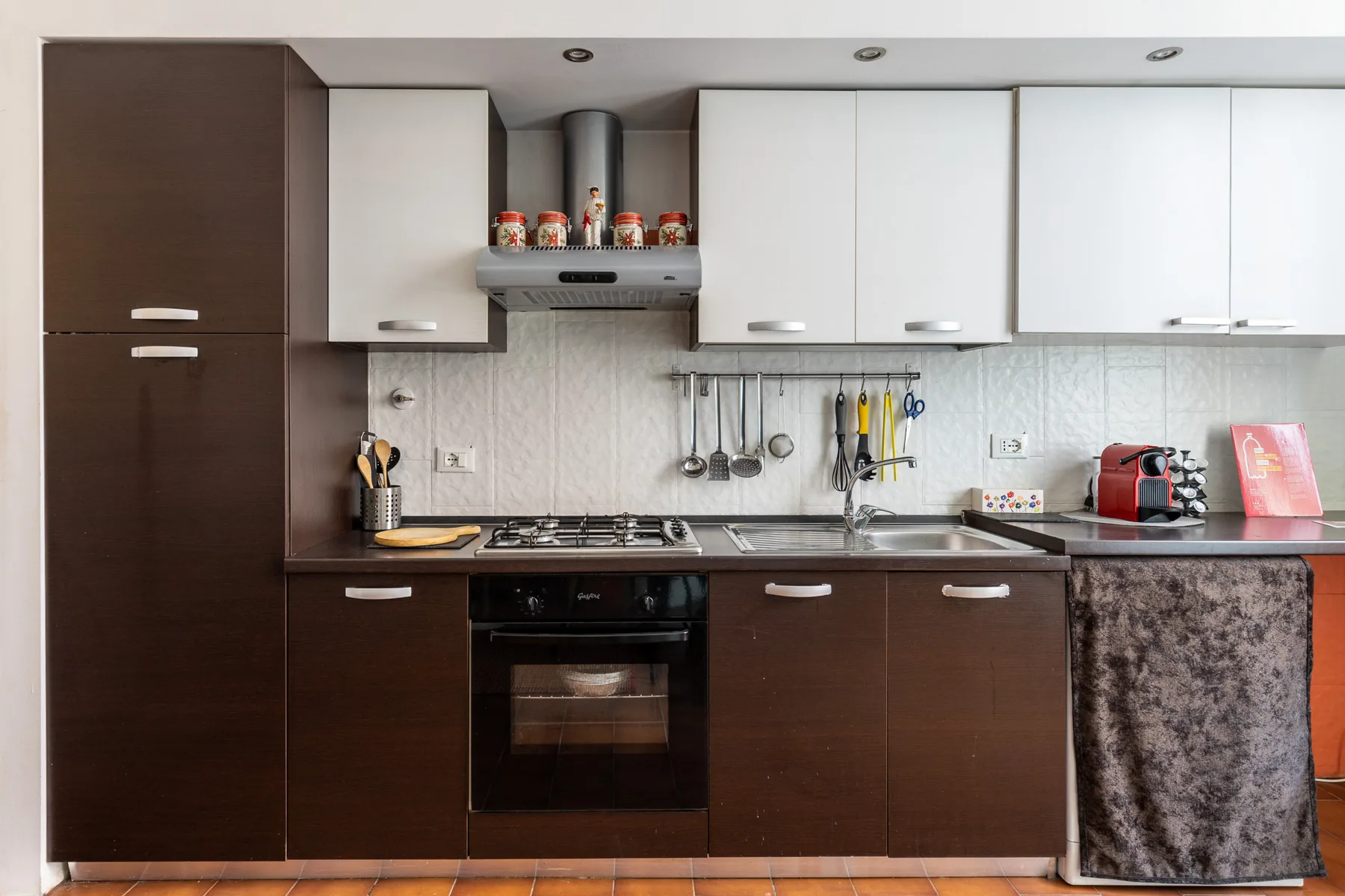 A modern kitchen with dark lower cabinets, light upper cabinets, and a stove.