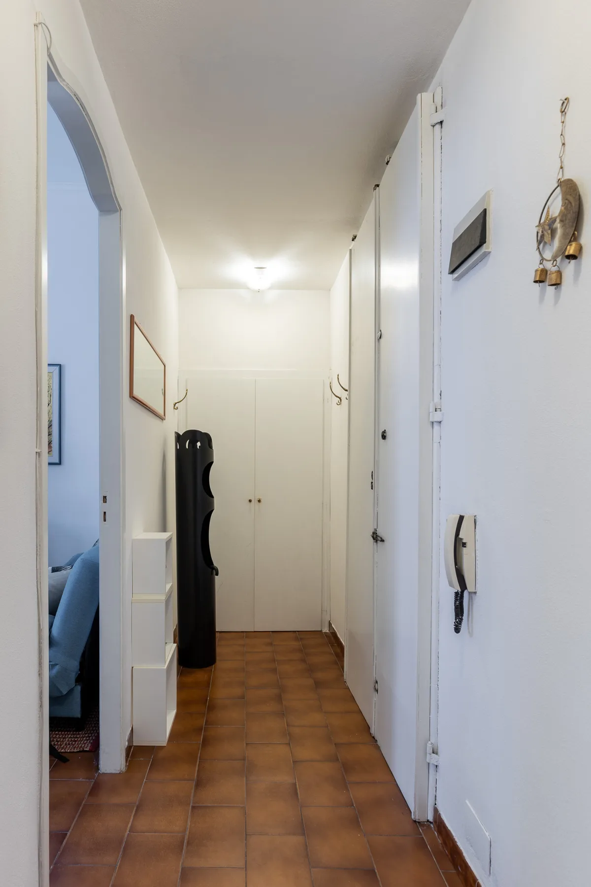 A narrow hallway with brown tile flooring and white doors.