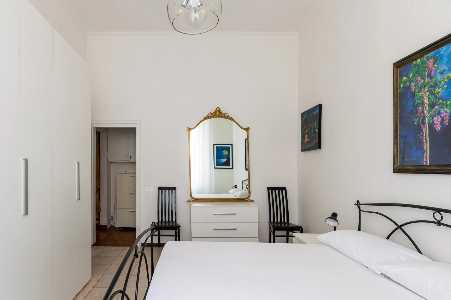 A bright bedroom with a made bed, a dresser, and framed artwork.