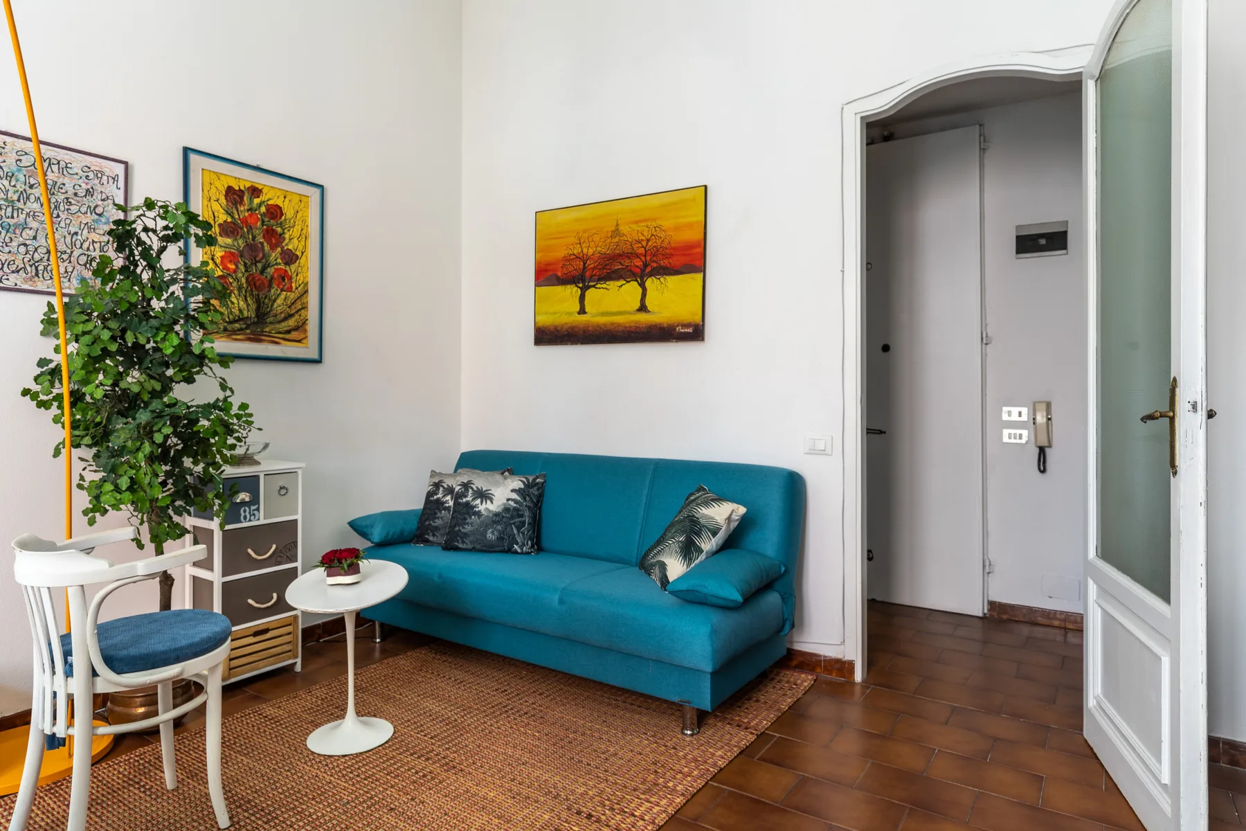 A living room with teal seating, a small table, and framed artwork.