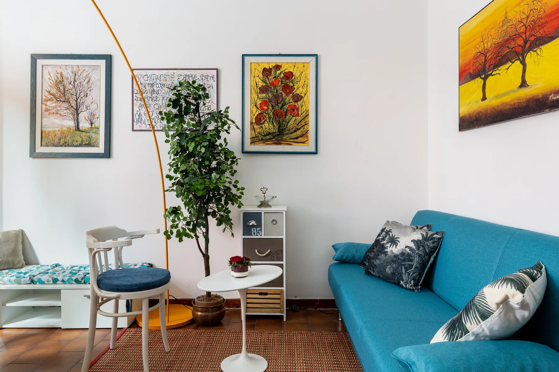A living room with a turquoise sofa, a small table, and framed artwork.