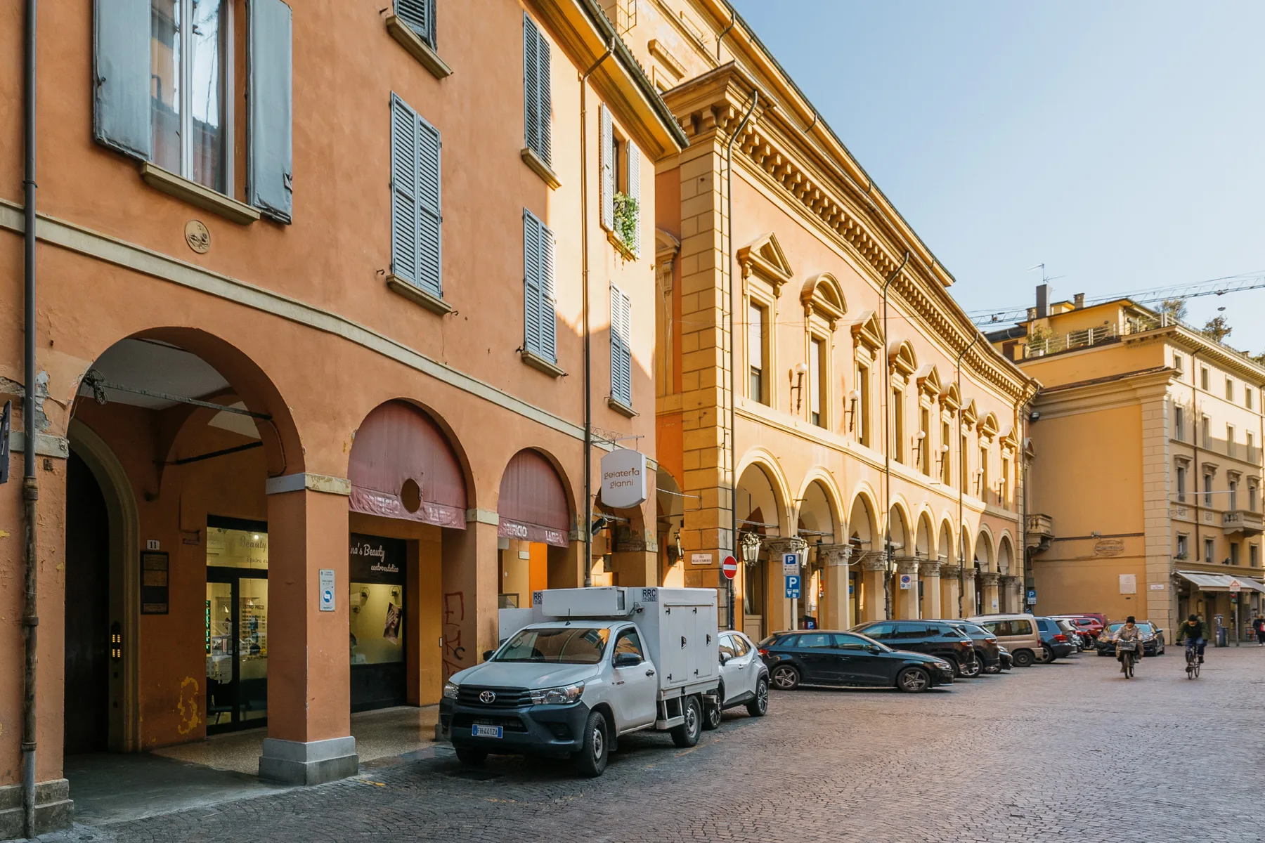A cobblestone street runs past colorful buildings with arched ground-floor openings.