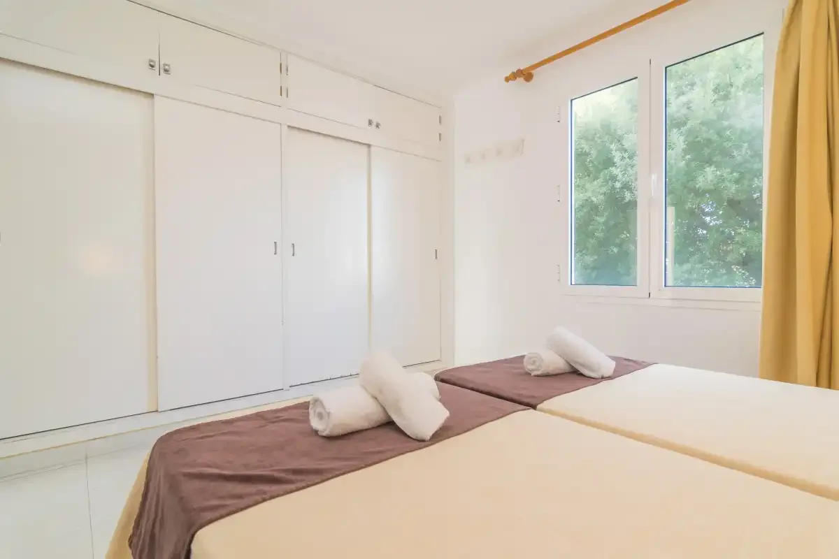 Un dormitorio luminoso con dos camas y ventanas grandes.