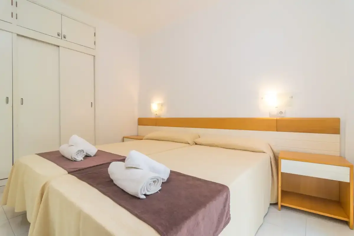 Un dormitorio luminoso con una cama doble, toallas dobladas y luces junto a la cama.