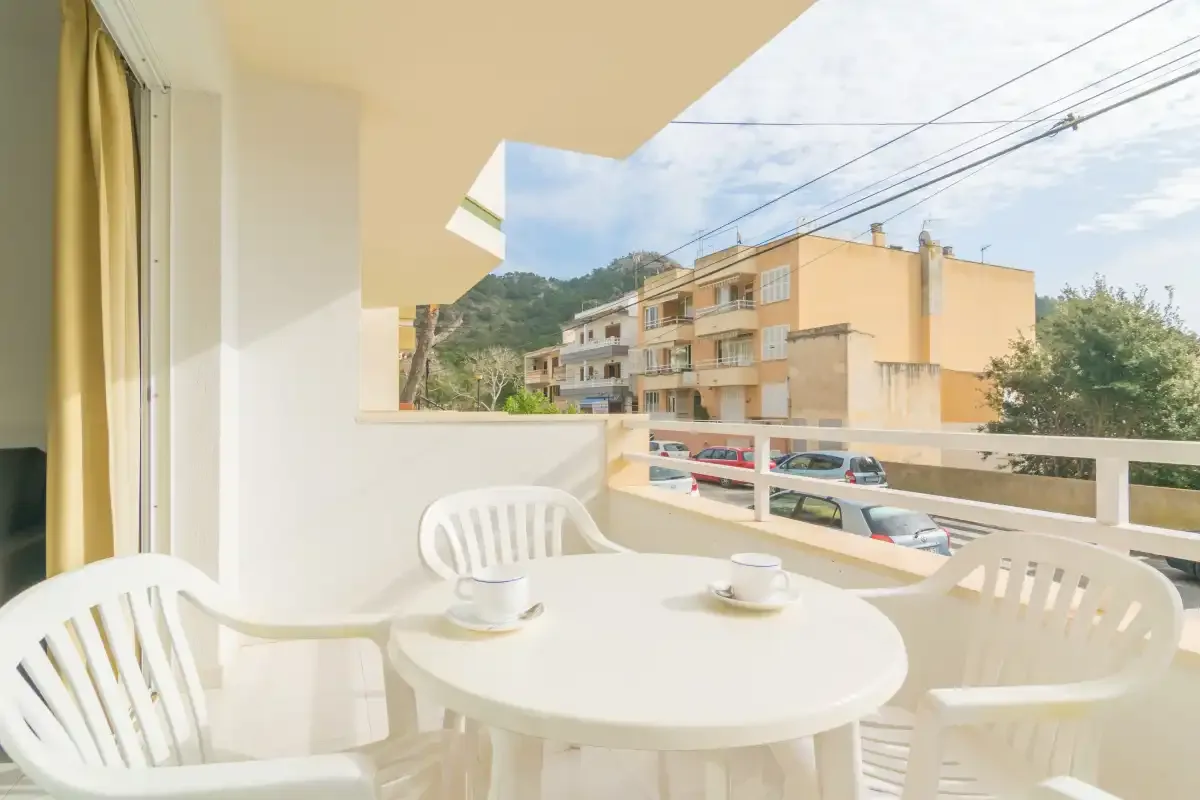 Una zona de estar en un balcón con mesa redonda mira hacia edificios y vegetación cercanos.