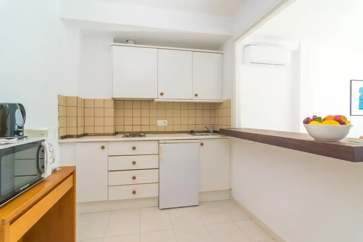 Una cocina compacta con armarios blancos, salpicadero de azulejos y una encimera.