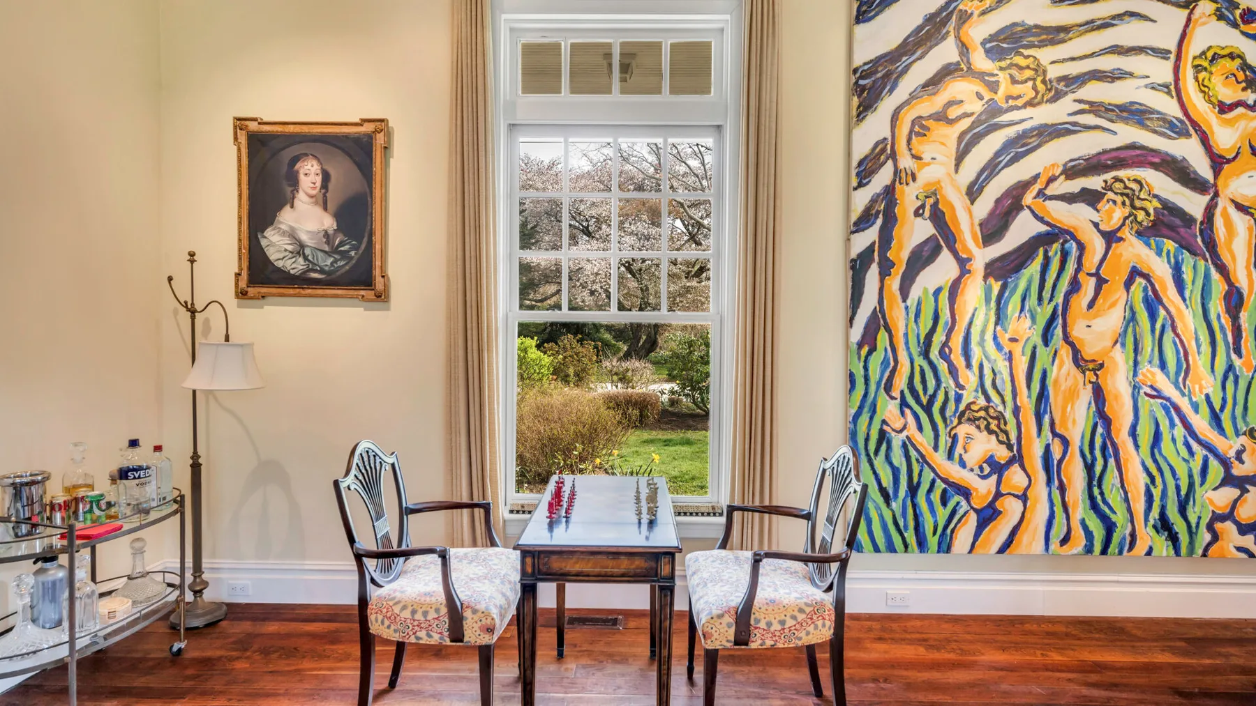Un comedor con una mesa y sillas junto a una ventana alta y una obra de arte colorida.