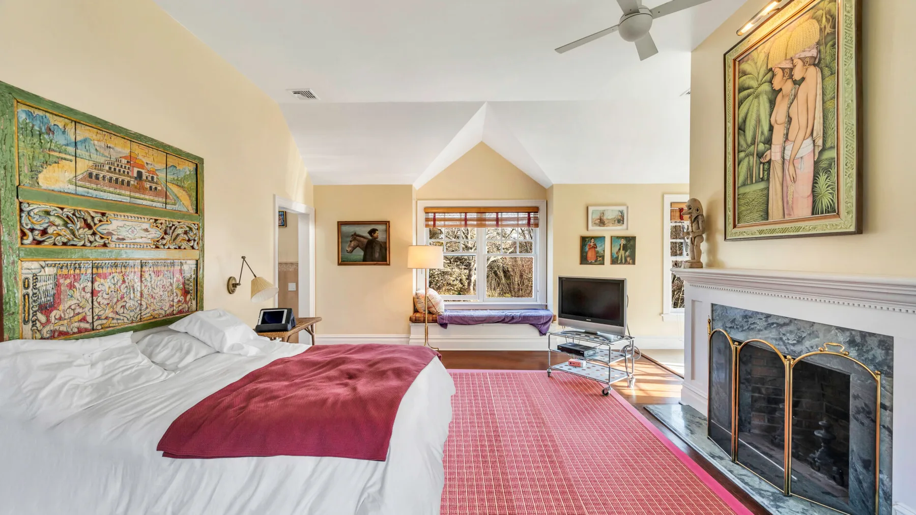Un dormitorio luminoso con una cama, una alfombra roja y una chimenea.