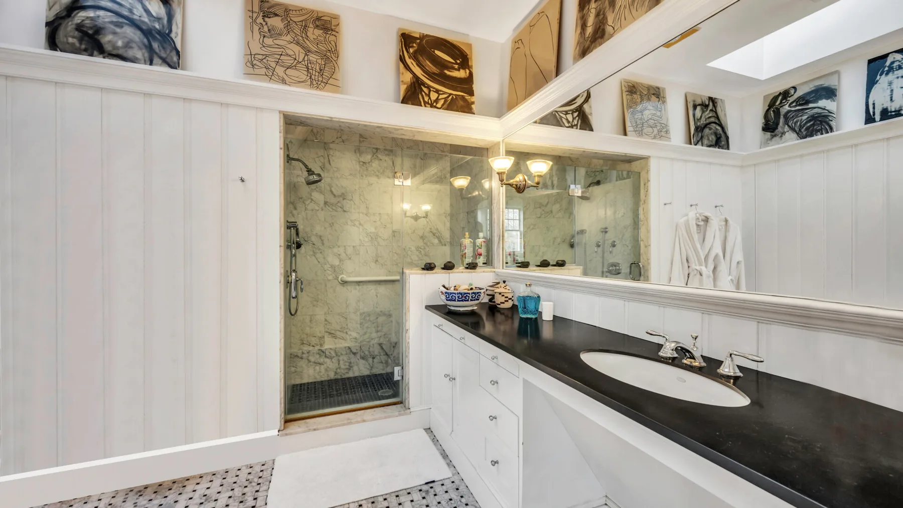 Un baño con una ducha de vidrio, una encimera oscura y un lavabo blanco.