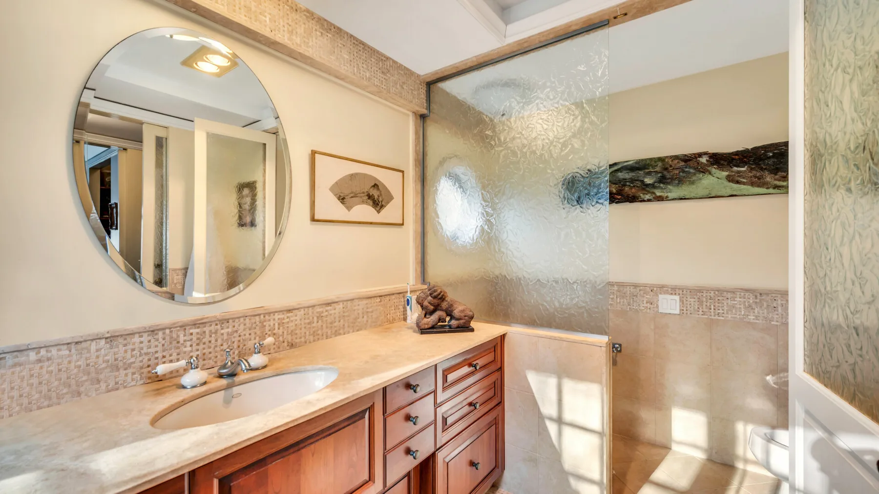 Un lavabo de baño con espejo redondo está junto a una mampara de vidrio esmerilado.