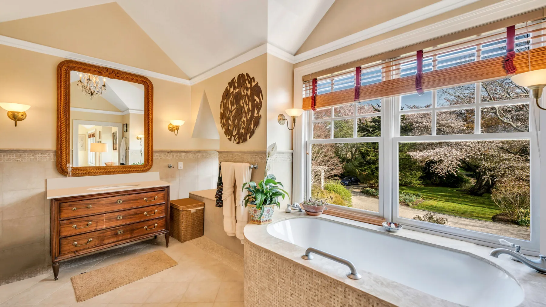 Un baño con una bañera bajo grandes ventanas con vistas a un jardín.