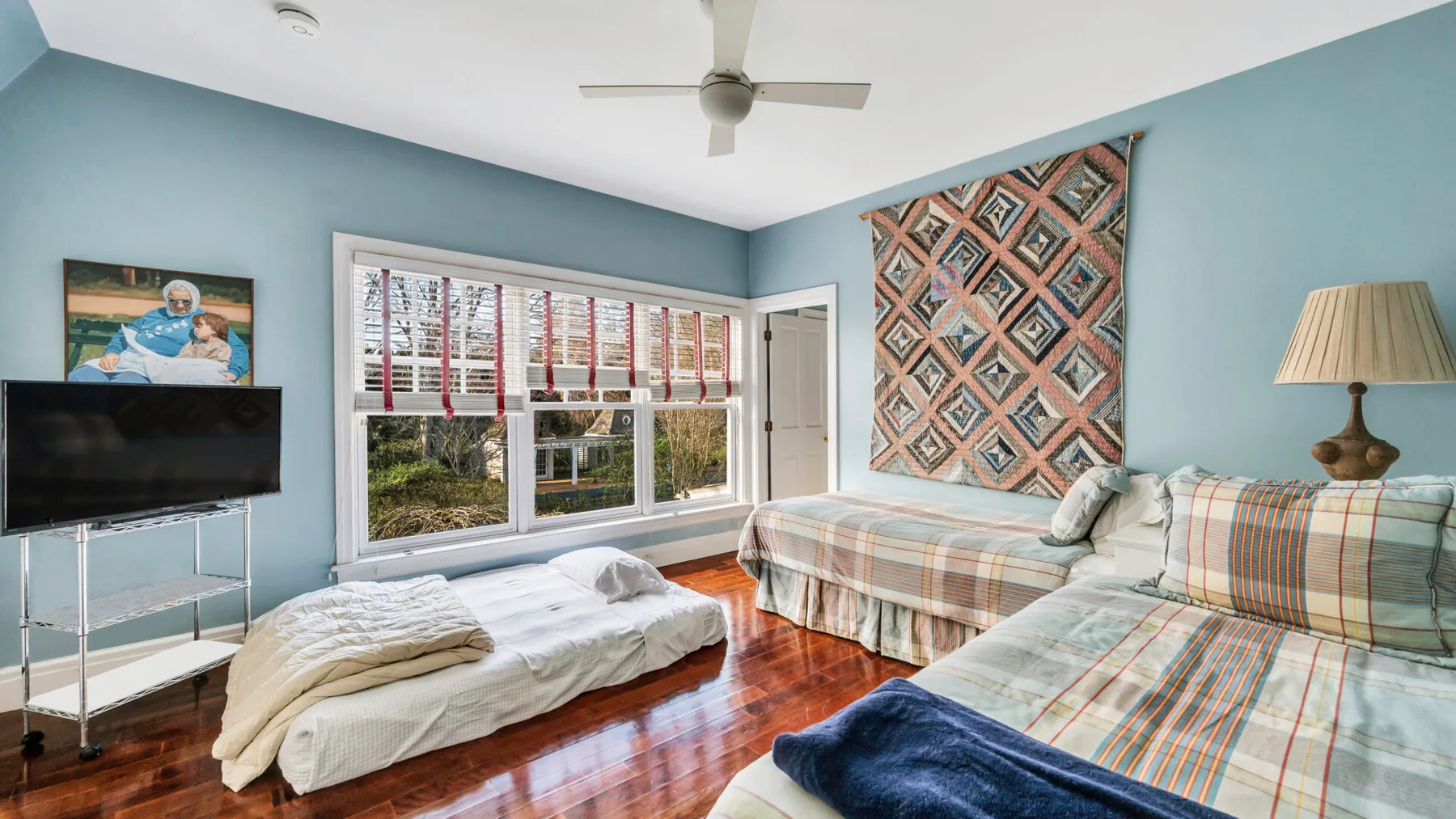 Un dormitorio azul con dos camas, un ventilador de techo y ventanas grandes.