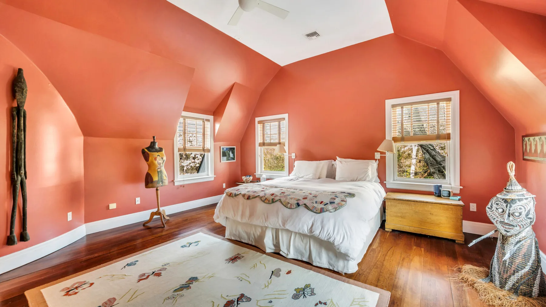 Un dormitorio con una cama grande, paredes color coral y varias ventanas.