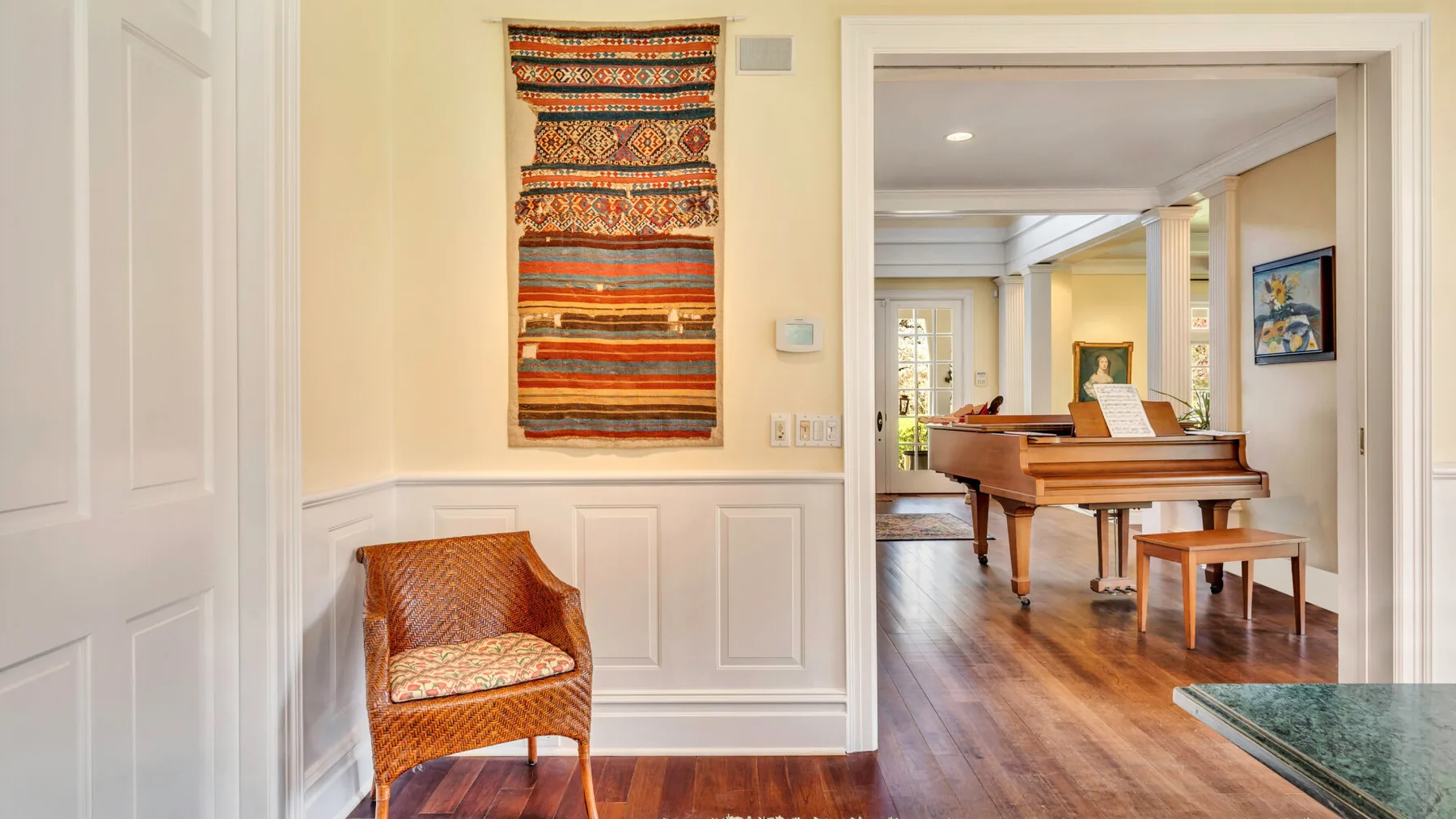 Un interior luminoso se abre a una habitación con un piano y asientos de mimbre.