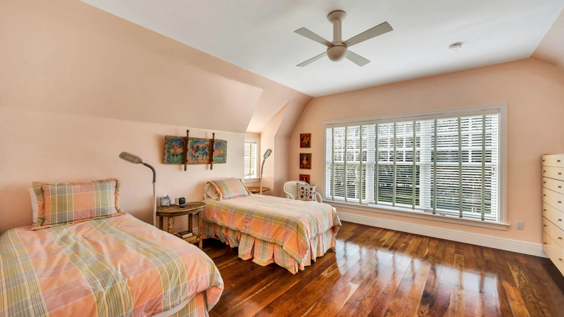 Un dormitorio luminoso con dos camas, ventanas amplias y suelo de madera pulida.