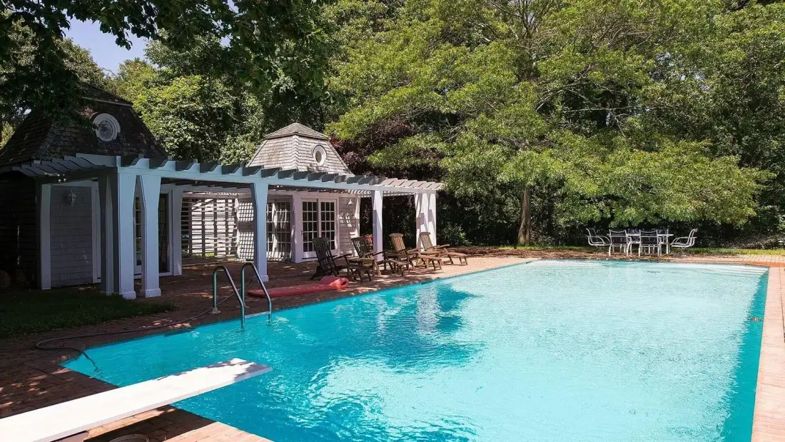 Una piscina junto a un patio sombreado con asientos al aire libre.