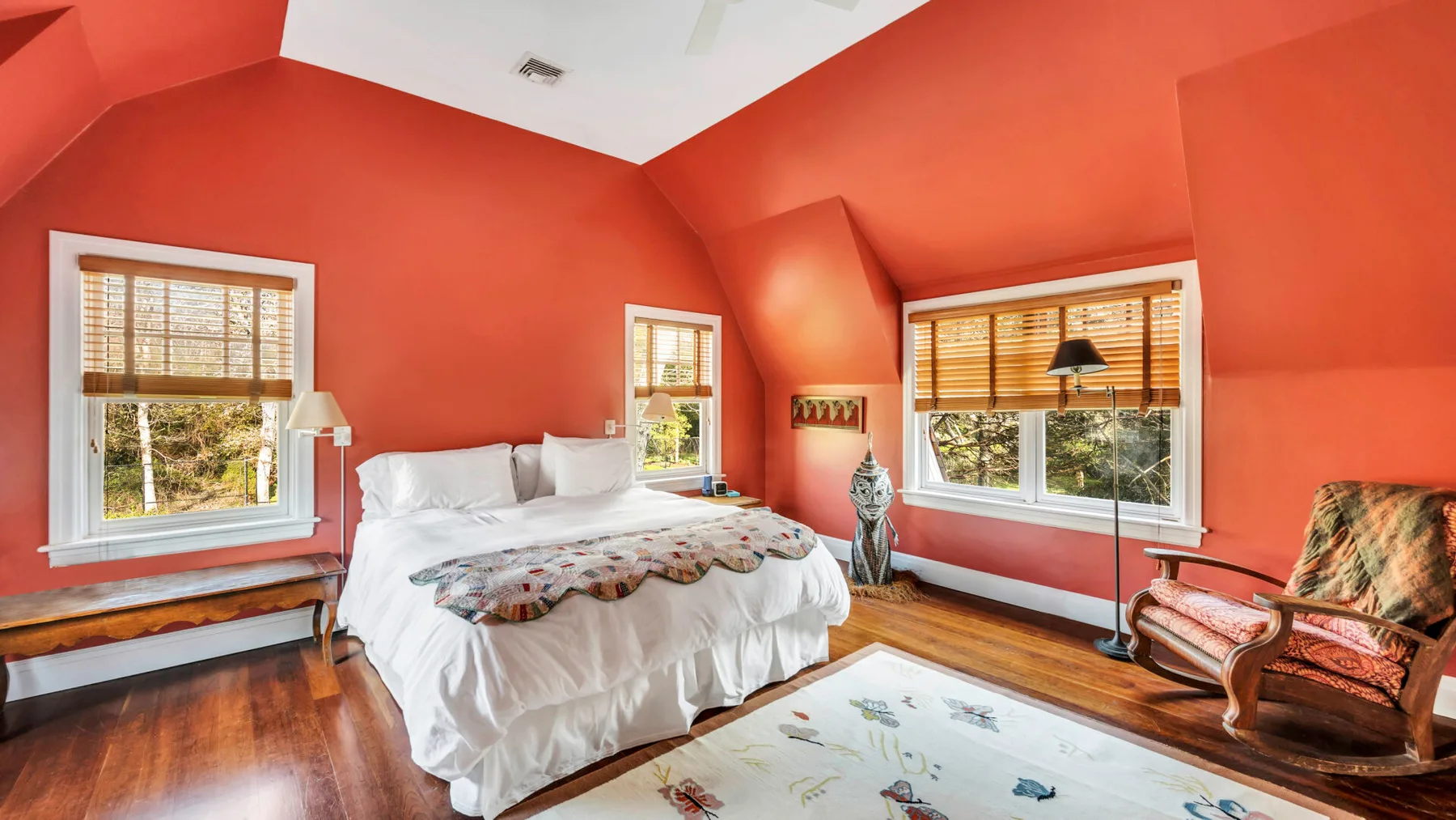 Un dormitorio con una cama, ventanas y paredes rojas cálidas.