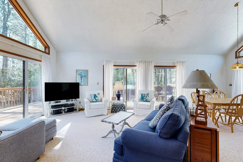 A bright living room with seating, large windows, and a dining area.