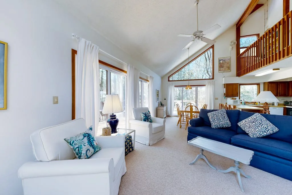 A bright living room with seating around a glass coffee table and dining area beyond.
