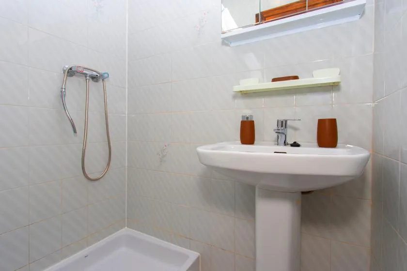 A tiled bathroom with a wall-mounted shower and pedestal sink.