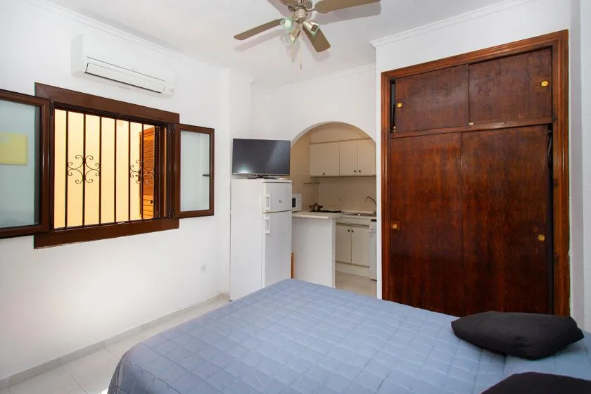A bedroom with a bed, a compact kitchen, and a wooden wardrobe.