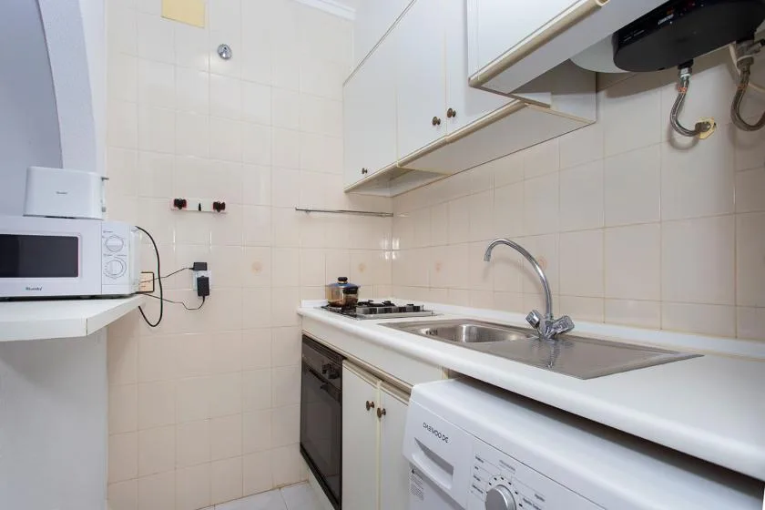 A compact kitchen with white cabinets, a sink, and a stovetop.