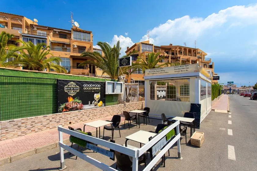 A street-side outdoor dining area with tables and chairs beside a restaurant.