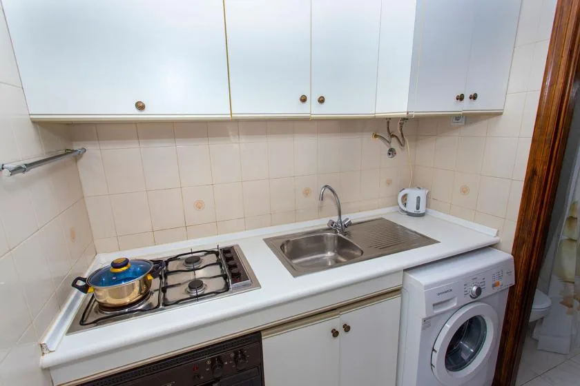 A compact kitchen with white cabinets, a sink, stovetop, and washing machine.