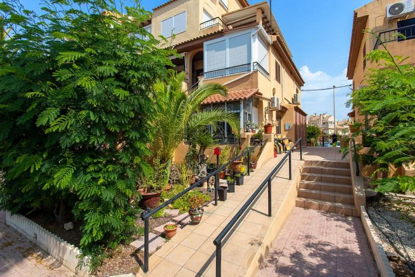 A residential building stands beside an outdoor ramp and steps, with greenery along the walkway.