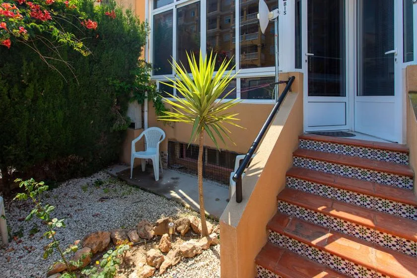 An outdoor entryway with tiled steps, a handrail, and surrounding greenery.