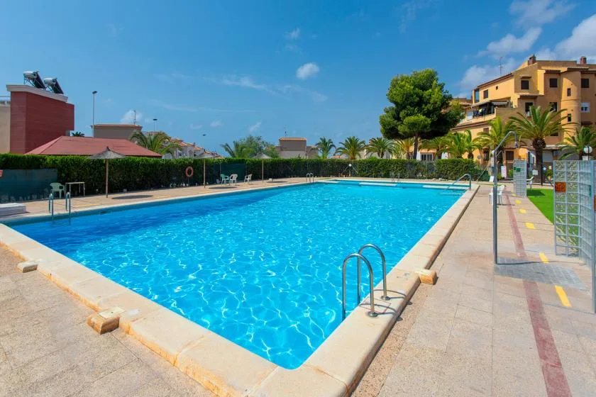 An outdoor swimming pool sits beside a paved walkway and landscaped grounds.