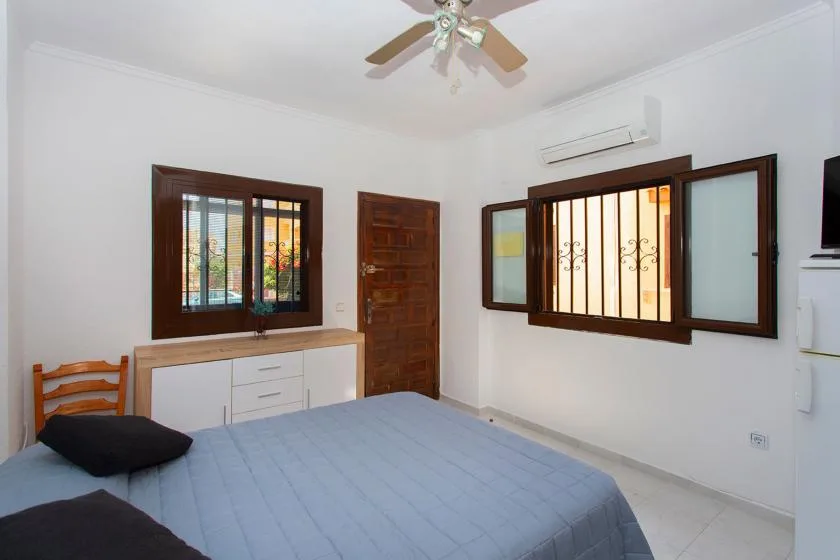 A bedroom with a blue-covered bed, windows, and a wooden door.