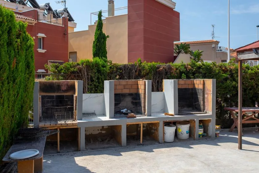 An outdoor barbecue area has built-in grills and a long counter.