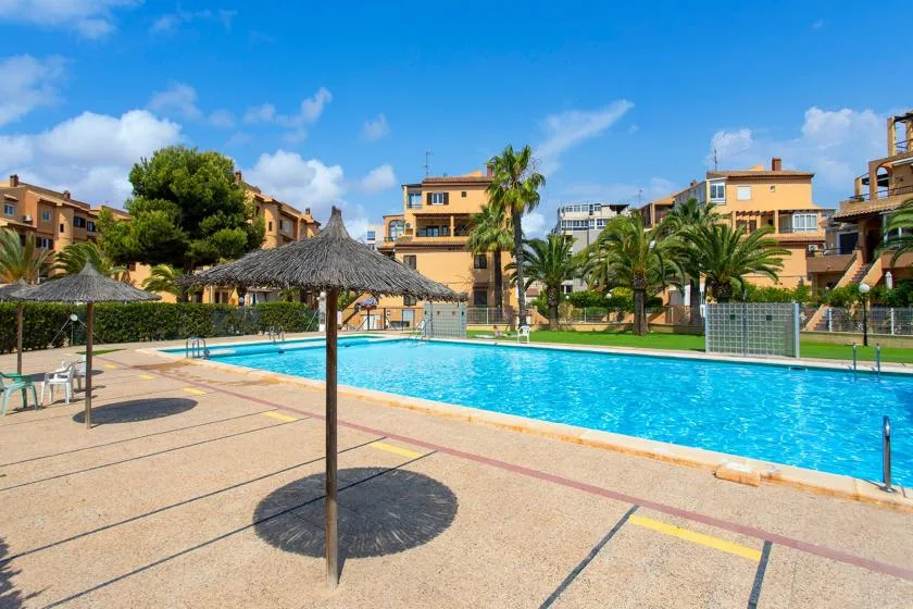 An outdoor swimming pool is surrounded by a paved deck and apartment buildings.