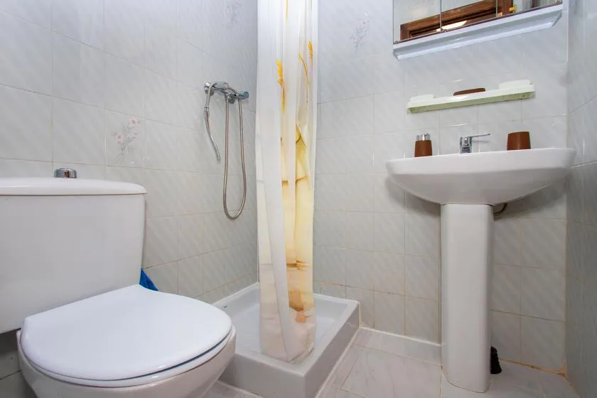 A tiled bathroom with a toilet, shower, and pedestal sink.