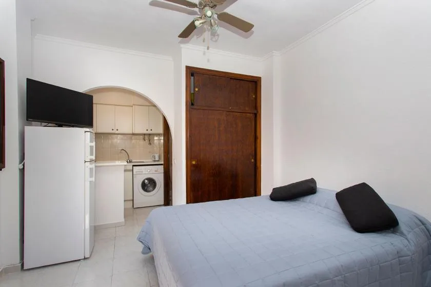 A bedroom with a bed, television, and compact kitchenette.