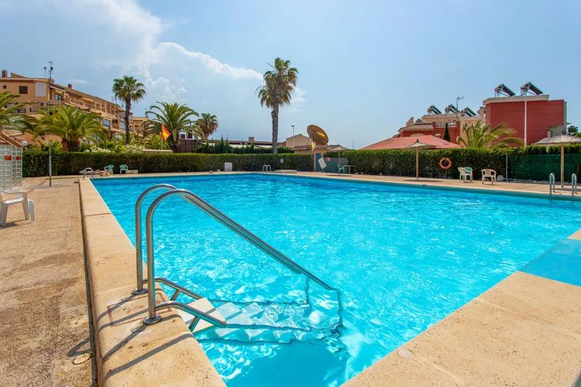 A swimming pool with steps and a metal handrail sits in a sunny outdoor area.