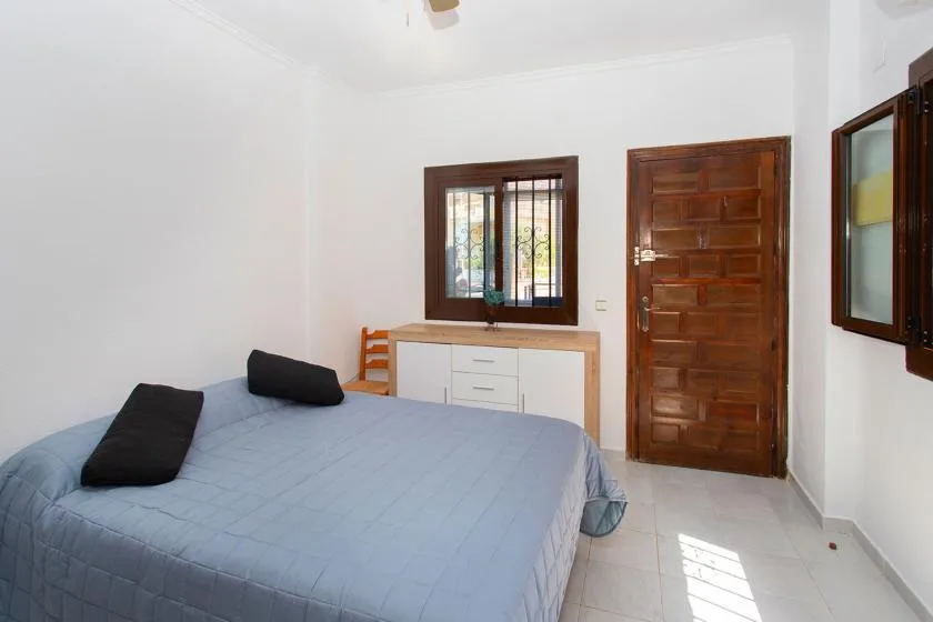 A bedroom with a bed, a dresser beneath the window, and a wooden door.