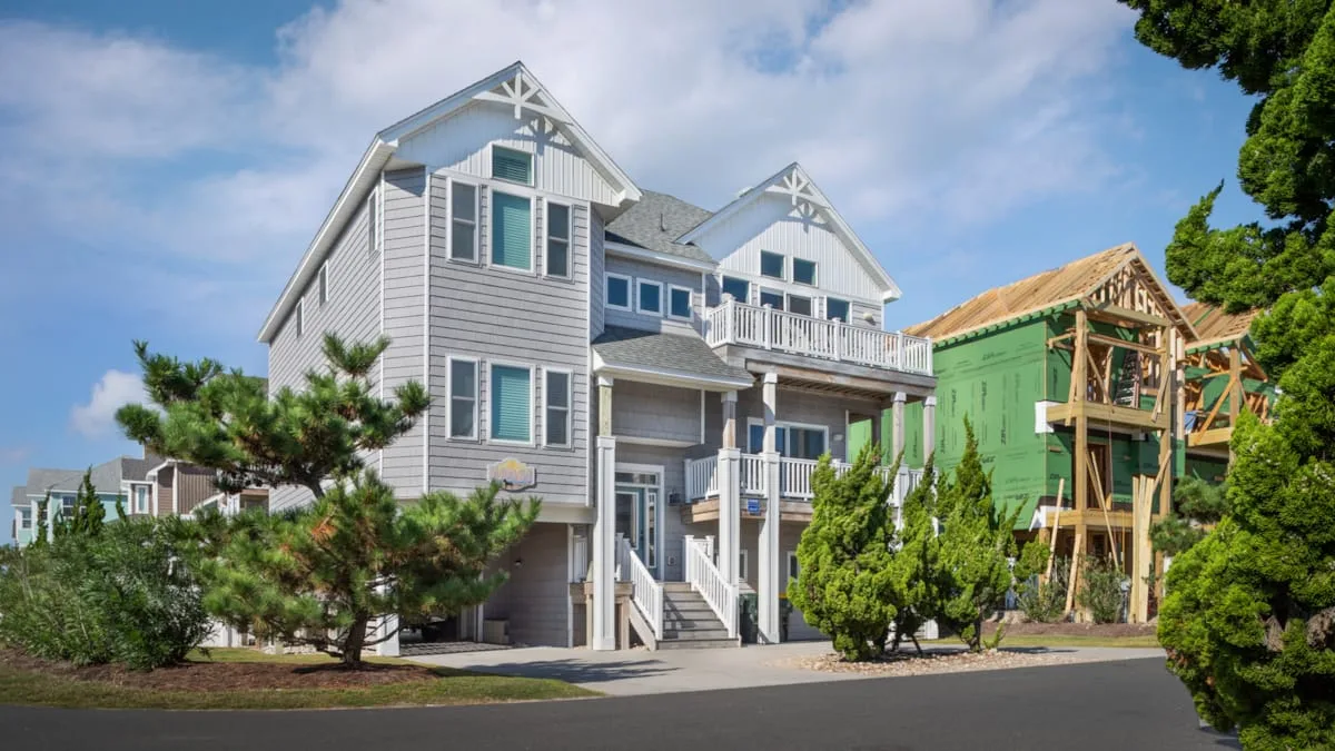 Una casa grande de color gris está junto a una vivienda vecina en construcción.